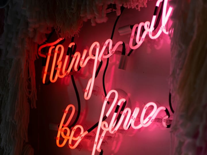 Neon lights sign in pink and red on a wall, stating "Things will be fine".